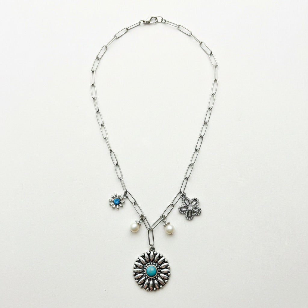 Silver necklace with floral and circular pendants on a light gray background
