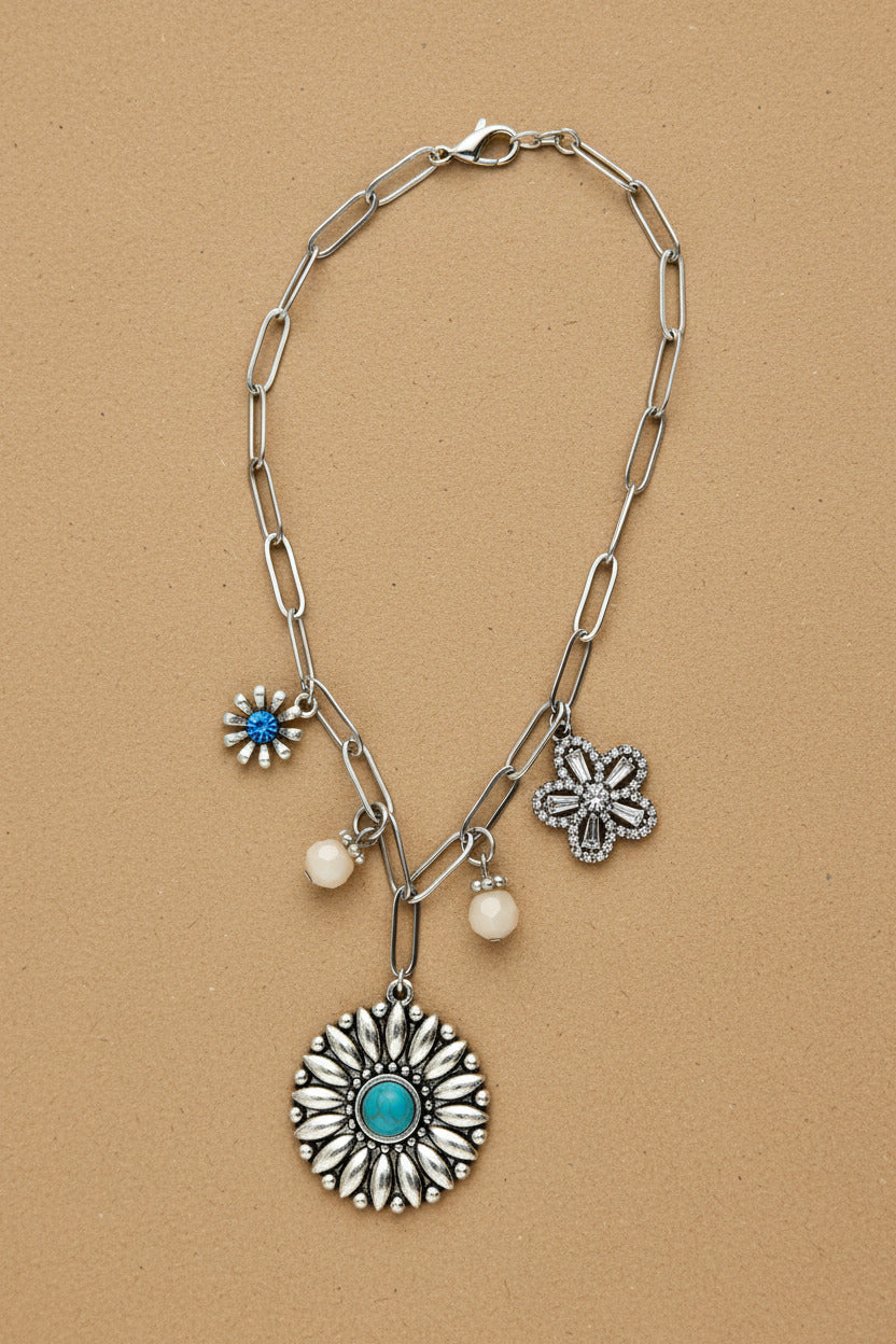Silver necklace with floral and round pendants on a light gray background