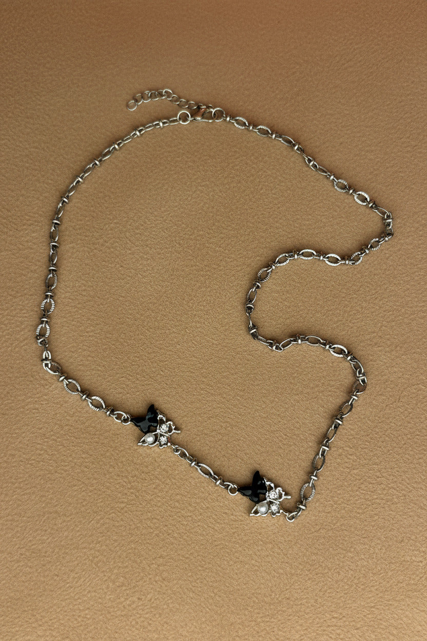 Silver necklace with buterfly and pear-shaped pendants on a light gray background