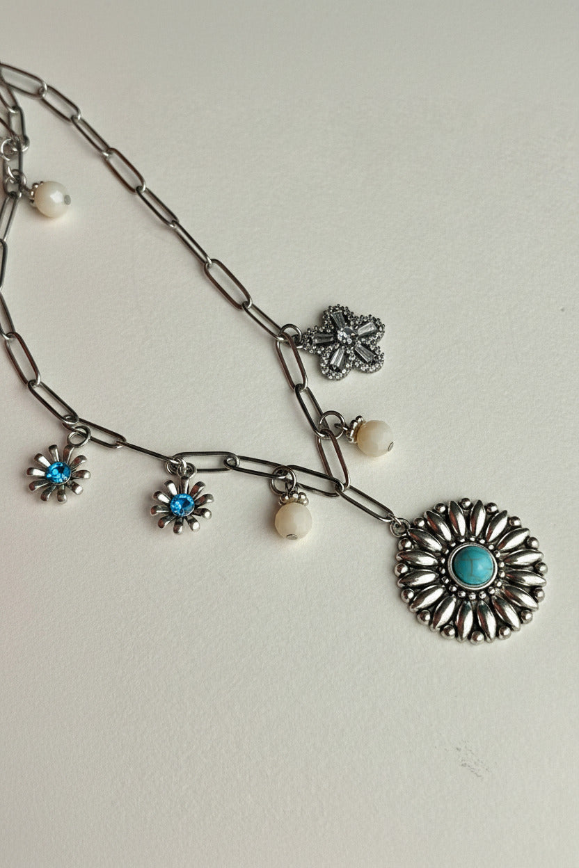 Silver necklace with floral and circular pendants on a light gray background