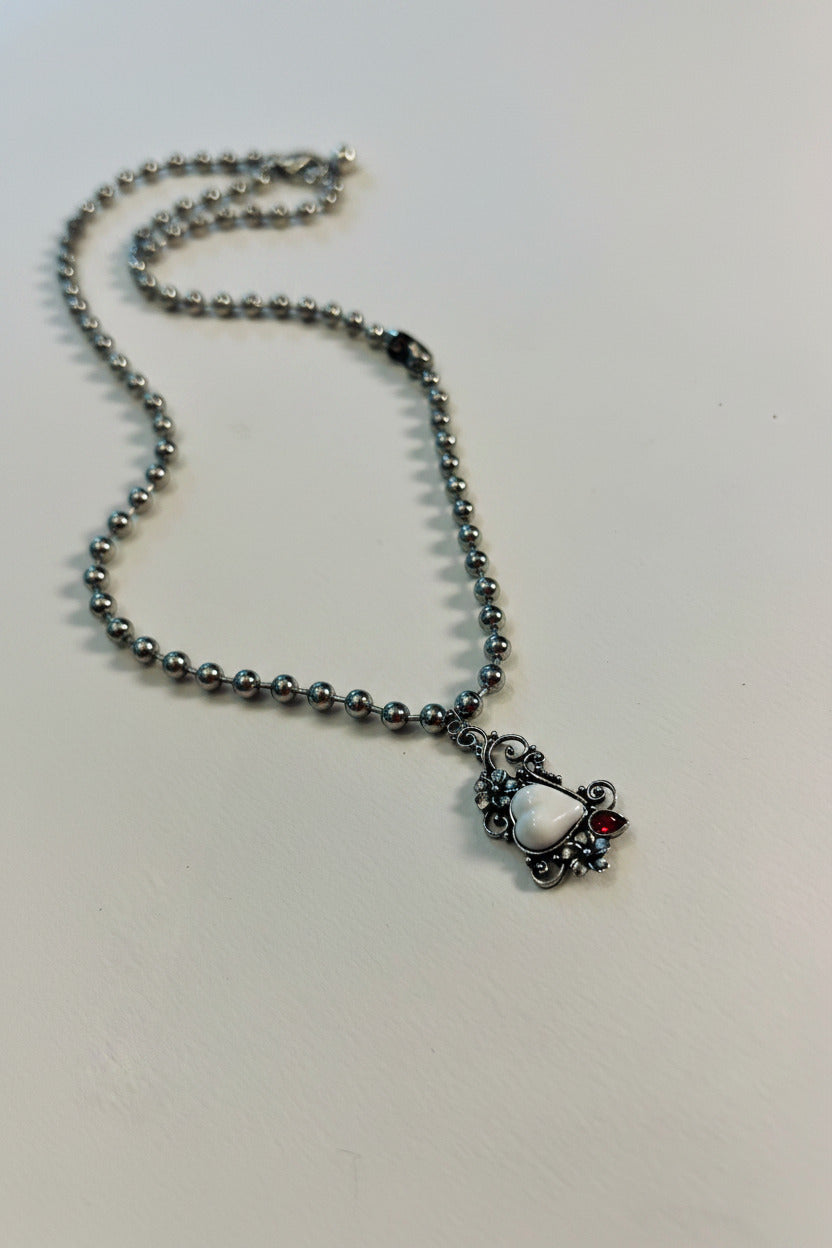 Necklace with a silver color pendant, white heart on a and red gem white background