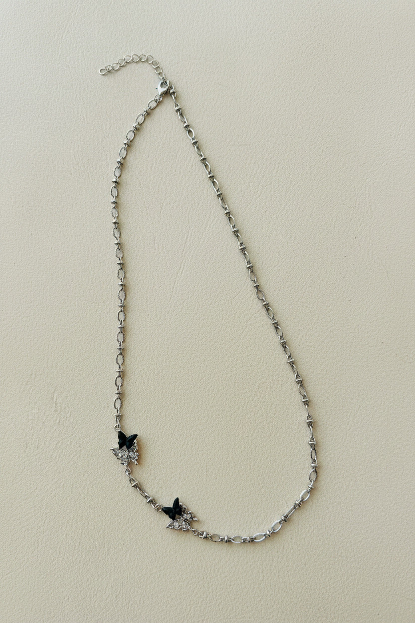 Silver chain necklace with black butterfly charms on a light gray background